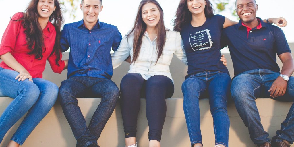 A young and diverse group smiling with arms around each other.