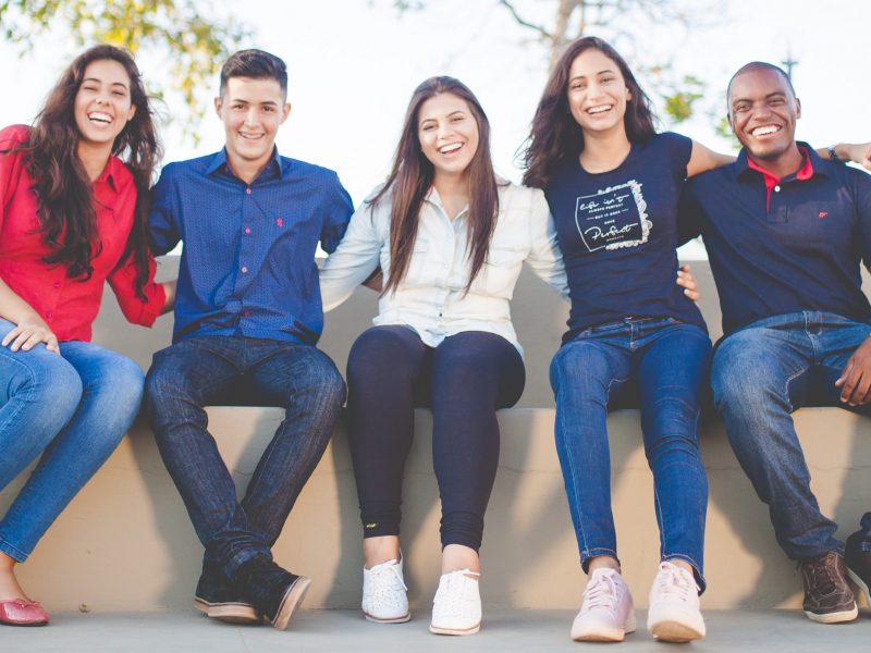 A young and diverse group smiling with arms around each other.