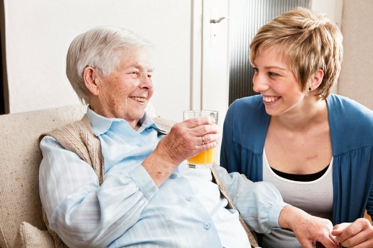 A middle aged woman smiling and holding hands with a elderly woman.