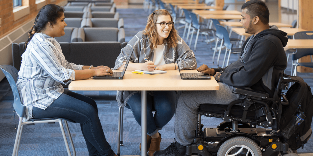 Three students working in front of laptops in a library setting.