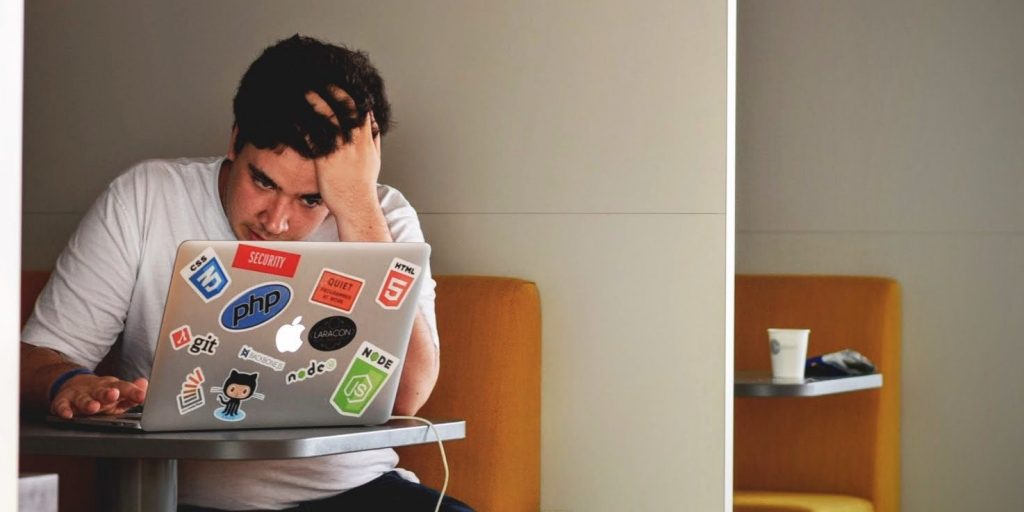 An individual stressfully holding their head up as they look at their laptop.