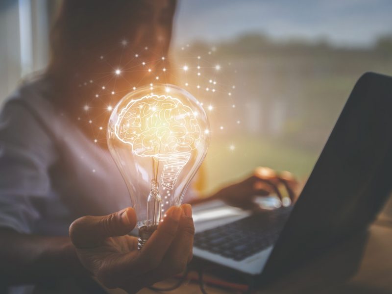 Individual working on her laptop while holding a lightbulb.