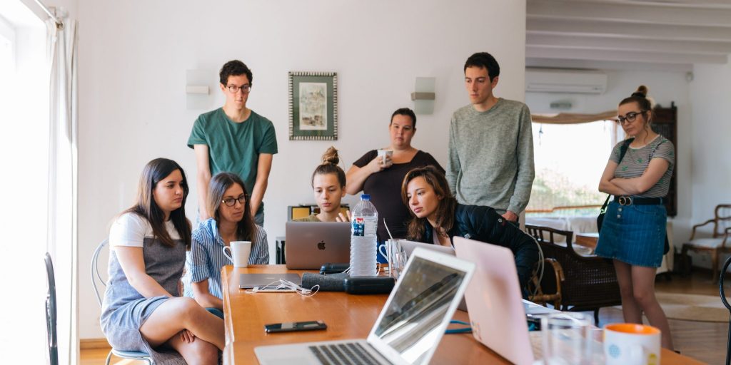 A group of people brainstorming and huddled over a laptop screen.