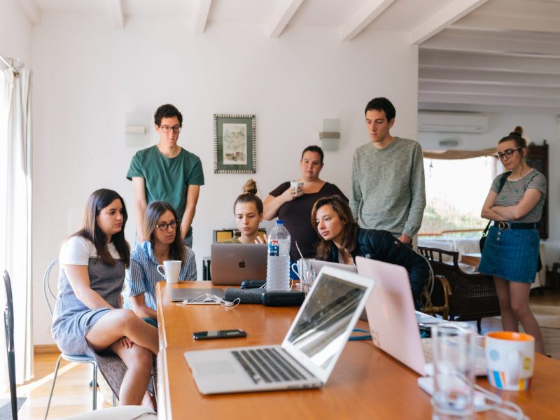 A group of people brainstorming and huddled over a laptop screen.