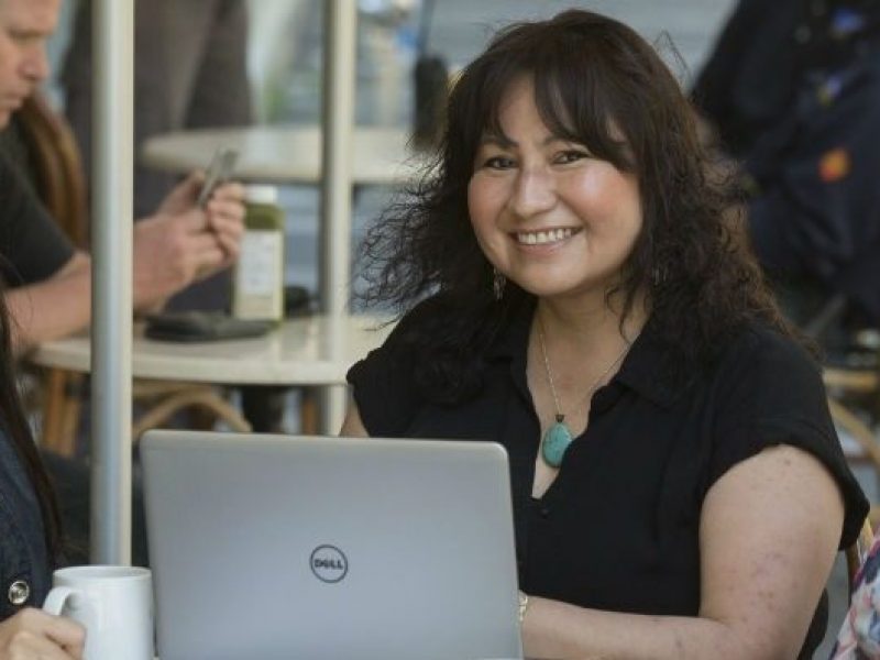 Three Indigenious women smiling and sitting in front of a laptop in a cafe setting.