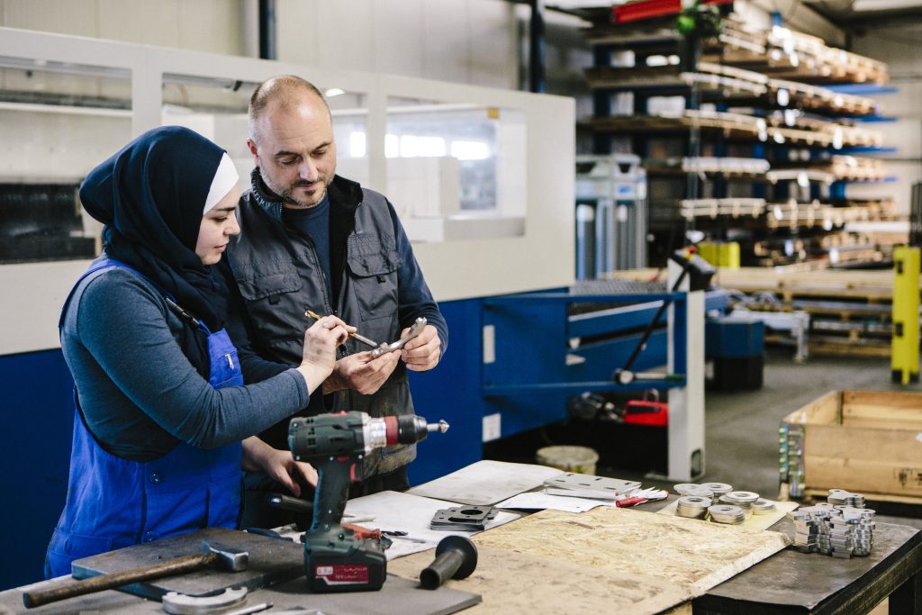 technician explains a work tool to a young woman in a workshop