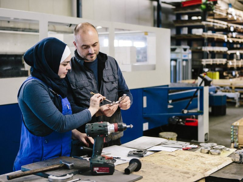 technician explains a work tool to a young woman in a workshop