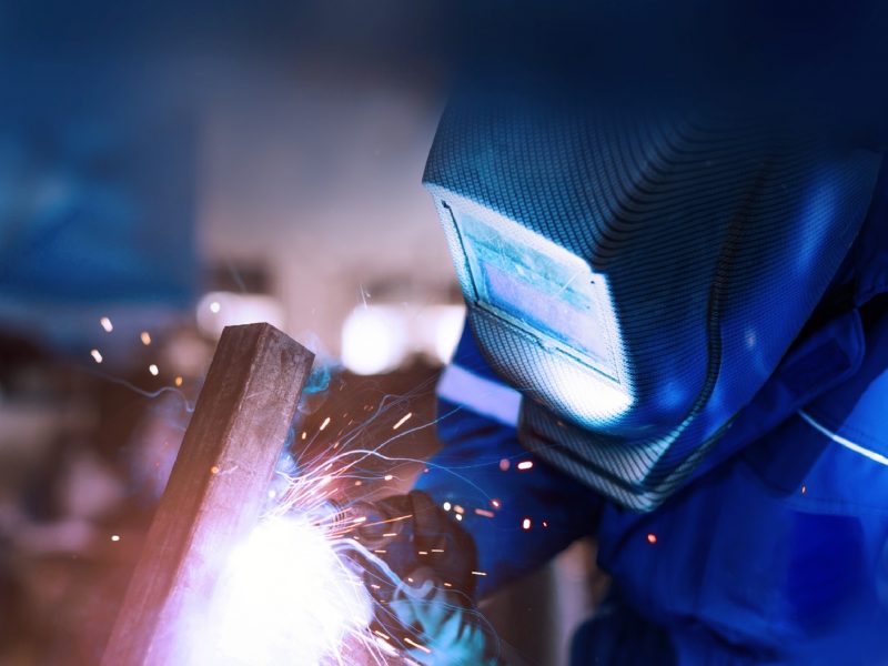 Worker wearing protective gear welding a metal pipe.