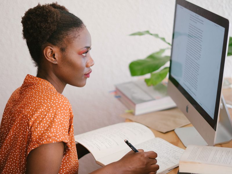 Employee taking hand-written notes while reading from a computer screen