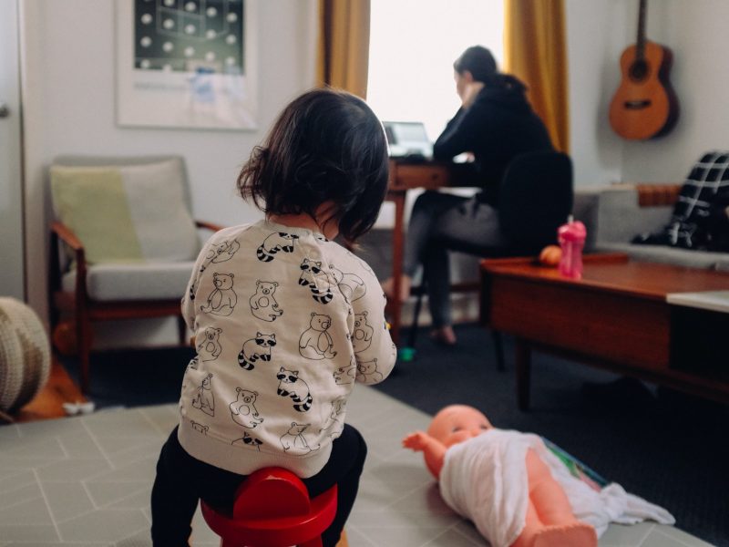 Professional mother working at home while her child is playing in the same room.