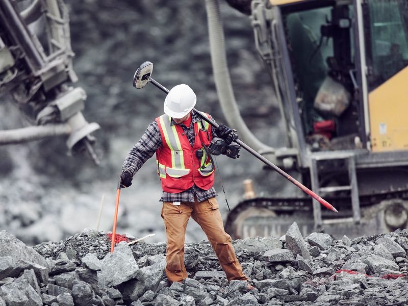 Miner performing a land survey with machinery behind him.