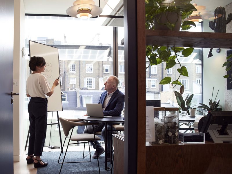 Person at whiteboard presenting to an individual with laptop