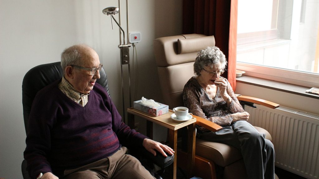 Two seniors sitting in armchairs in a hospital setting