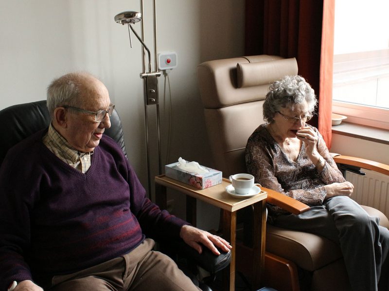 Two seniors sitting in armchairs in a hospital setting