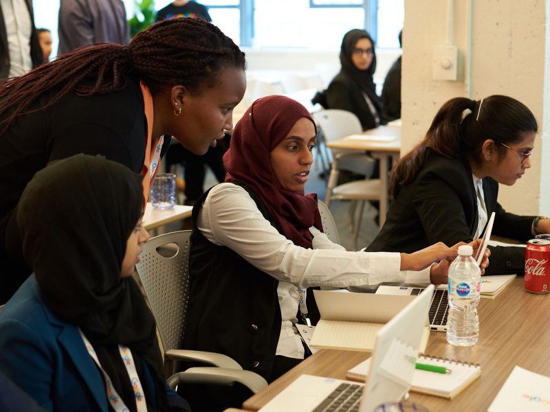 Diverse youth working on laptop; person leaning in to provide support