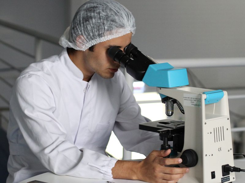 Scientist looking through compound microscope 