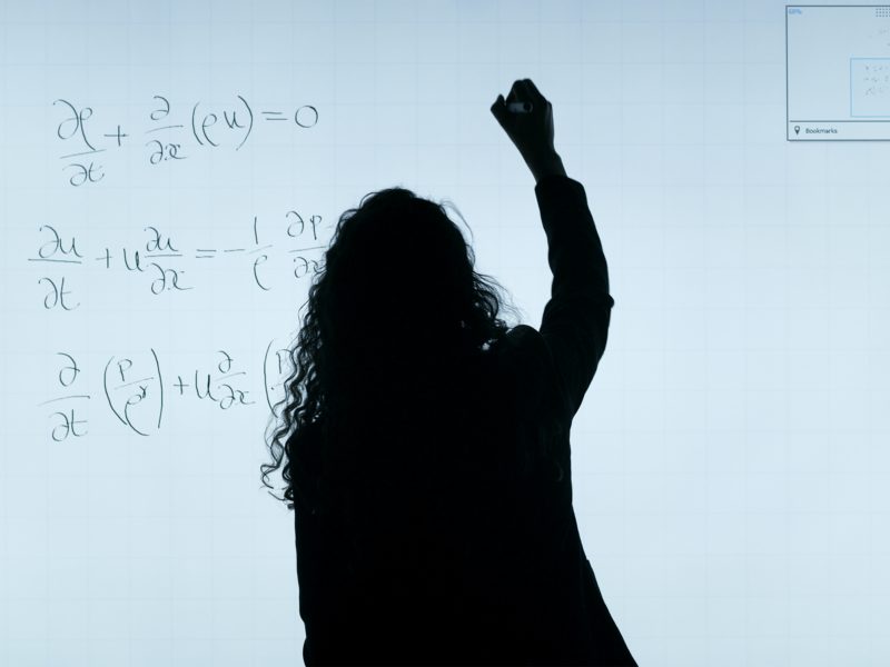 Silhouette of a woman completing a mathematics question on a white board