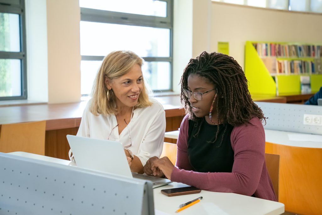 Two women looking at a laptop in a library.