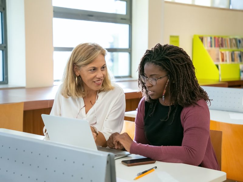 Two women looking at a laptop in a library.