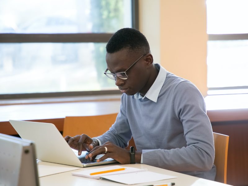 Young student using a laptop and taking notes in a library.