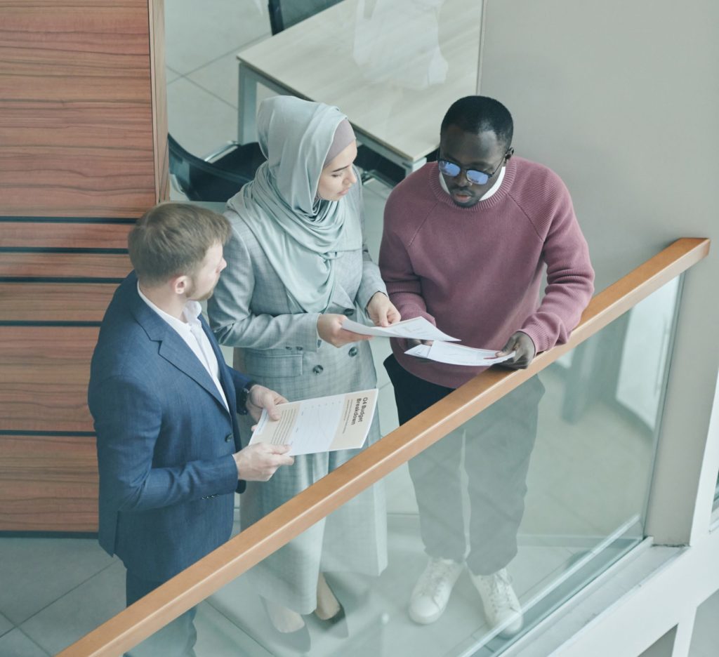 Two men and a woman looking at documents and discussing in a hallway.