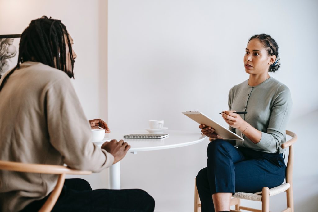 Two individuals sitting across from eachother discussing with a notepad.