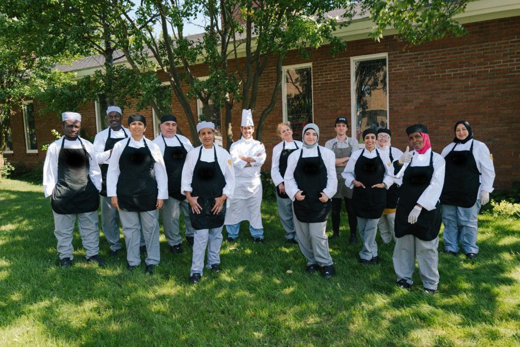Group of diverse individuals wearing chef clothing in a class photo.