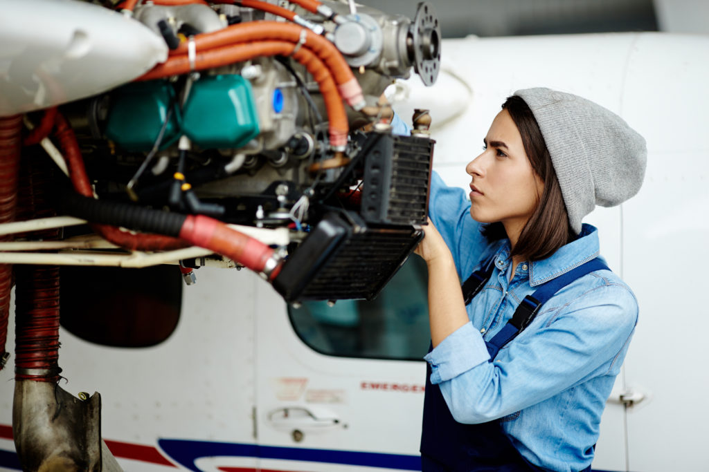 Young woman repairing airplane motor.