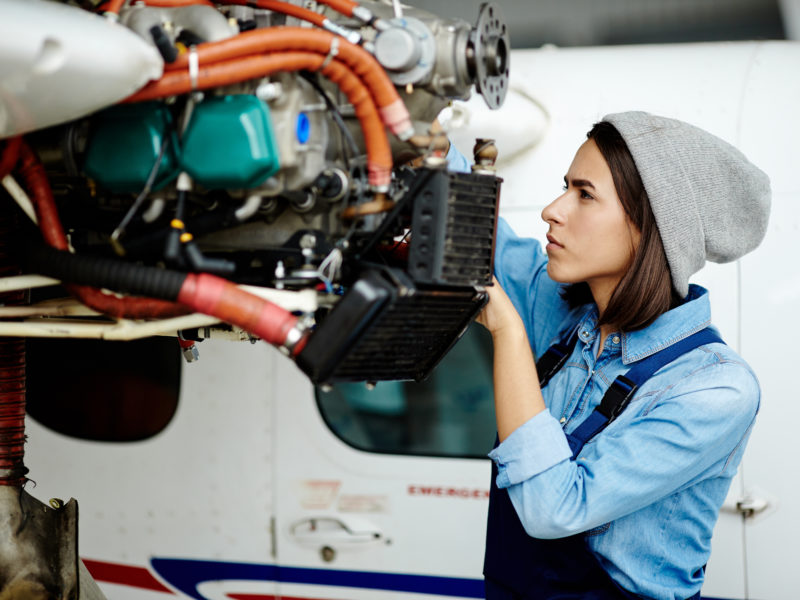 Young woman repairing airplane motor.