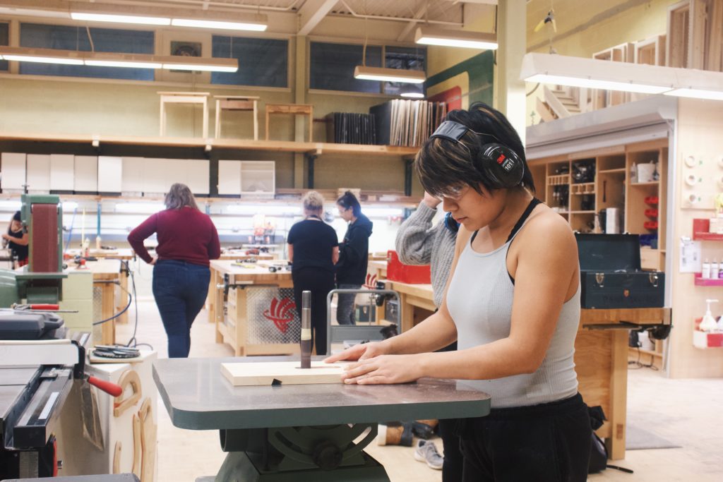 Young girl with headphones using a bandsaw in woodworking class.