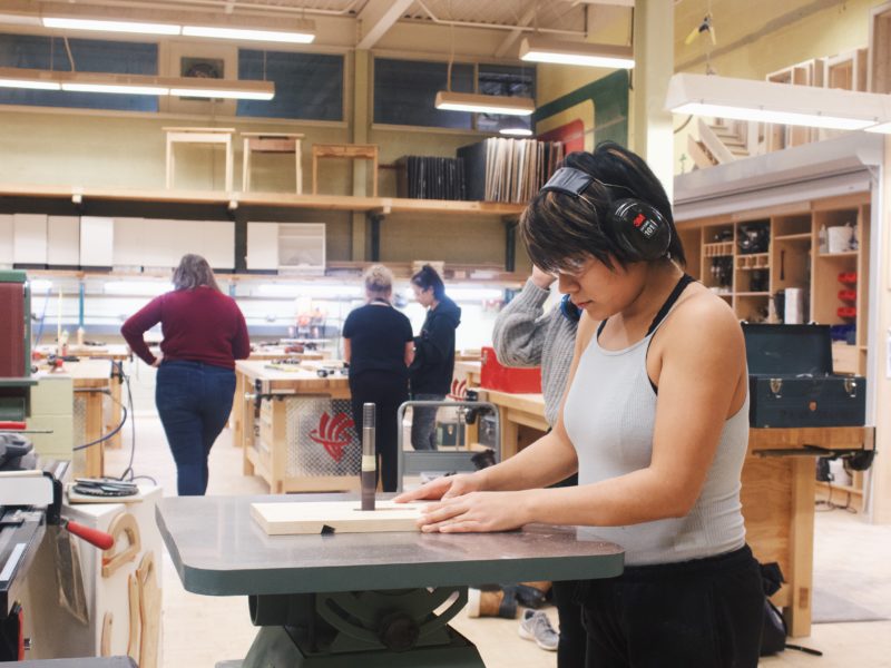 Young girl with headphones using a bandsaw in woodworking class.