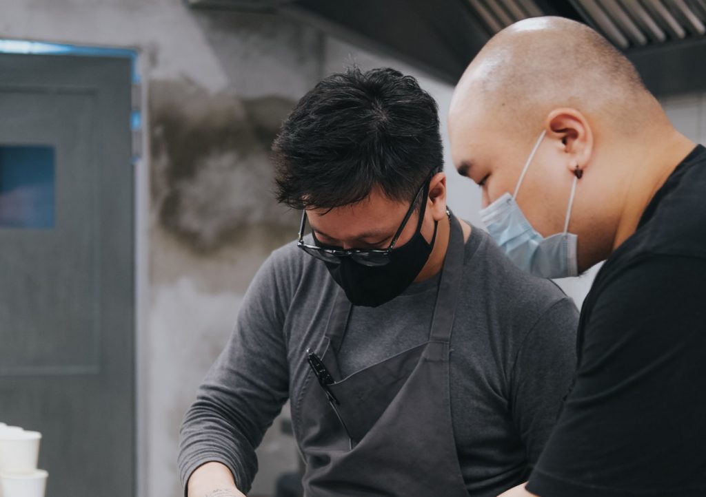 Two men packaging containers in a restaurant kitchen.