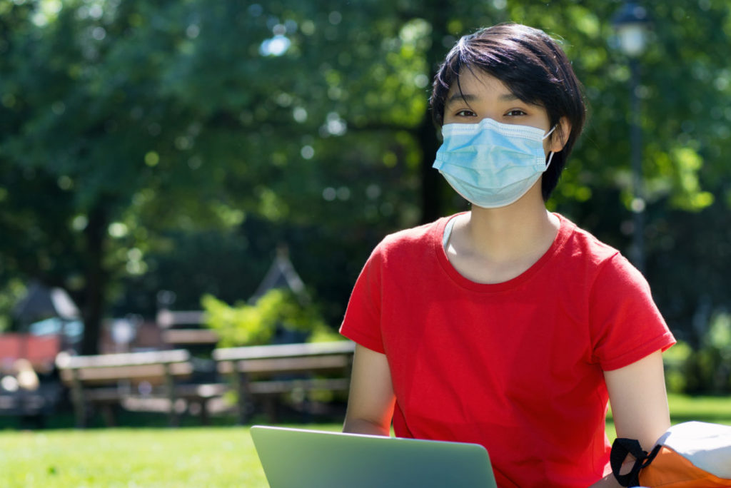 Student sitting outside of university campus with a clinical mask on.