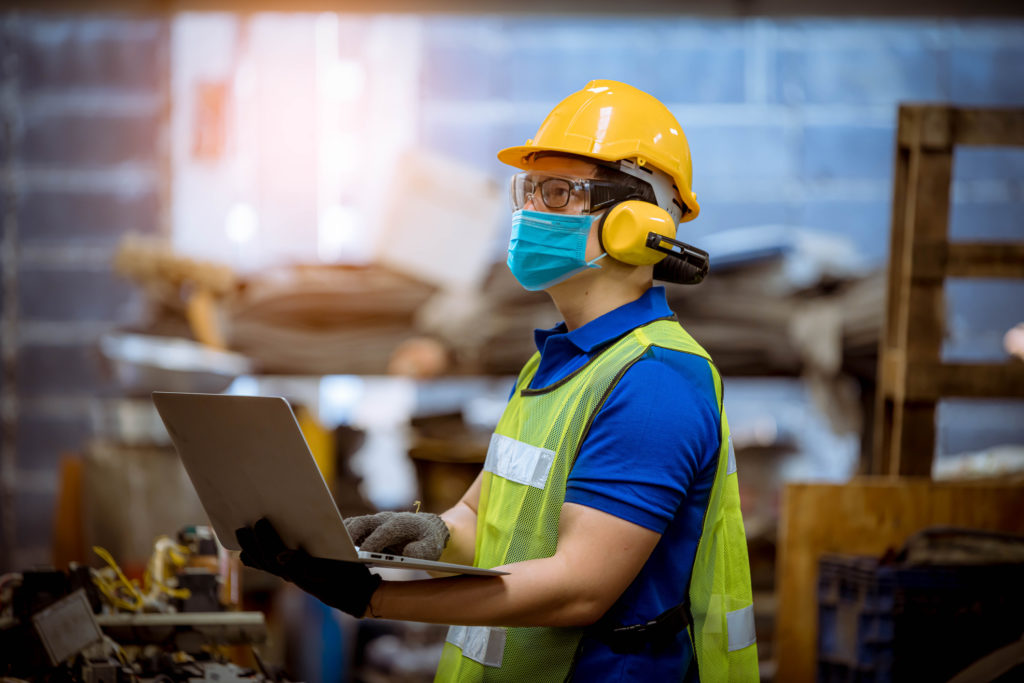 Construction worker holding laptop and wearing a clinical mask.