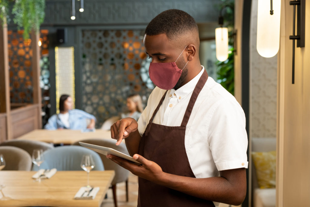 A server taking an order in a restaurant with a face mask on.