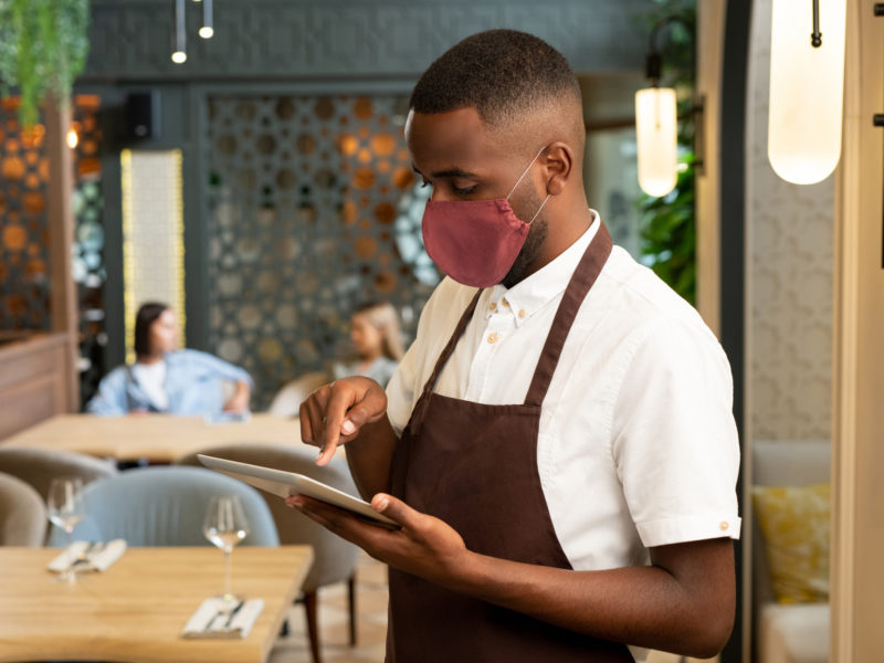 A server taking an order in a restaurant with a face mask on.