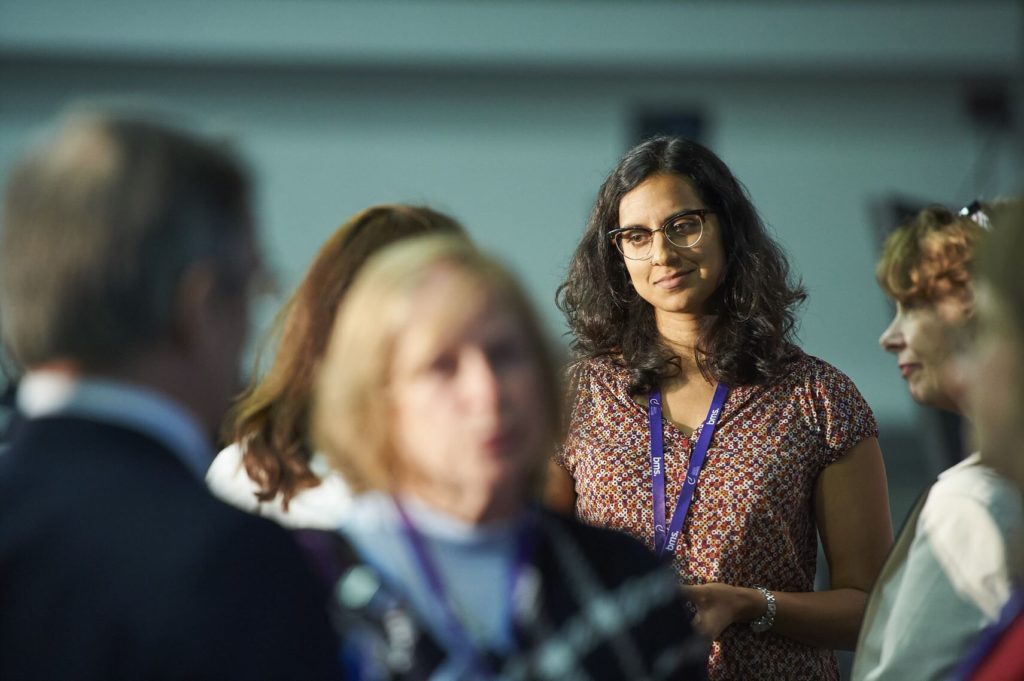 Group of individuals with one woman in focus standing in a conference hall.