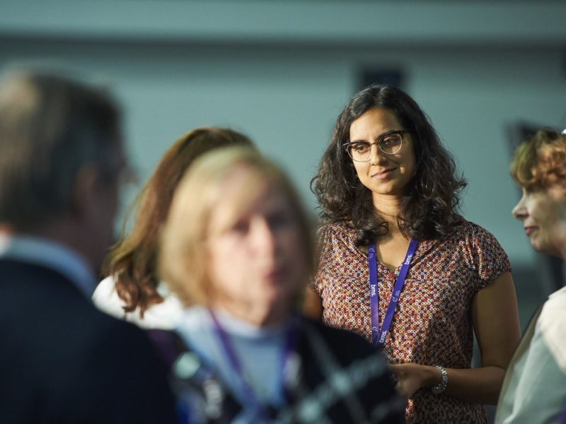 Group of individuals with one woman in focus standing in a conference hall.