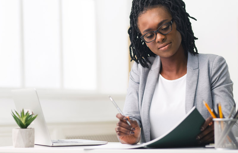 Woman in blazer writing in notebook.