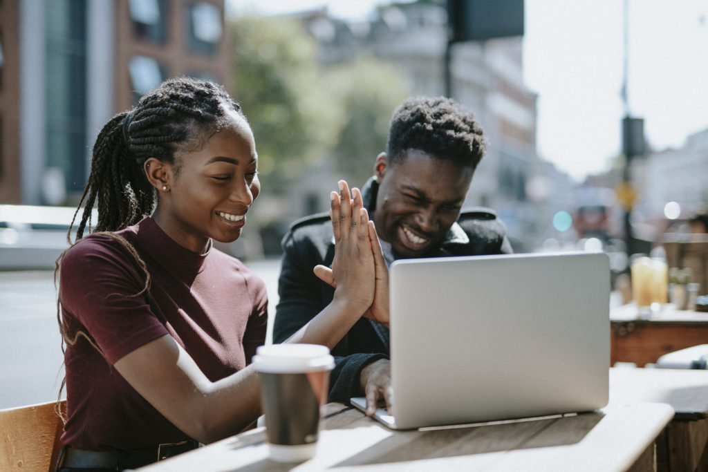 Two young individuals high fiving while they work on a laptop.