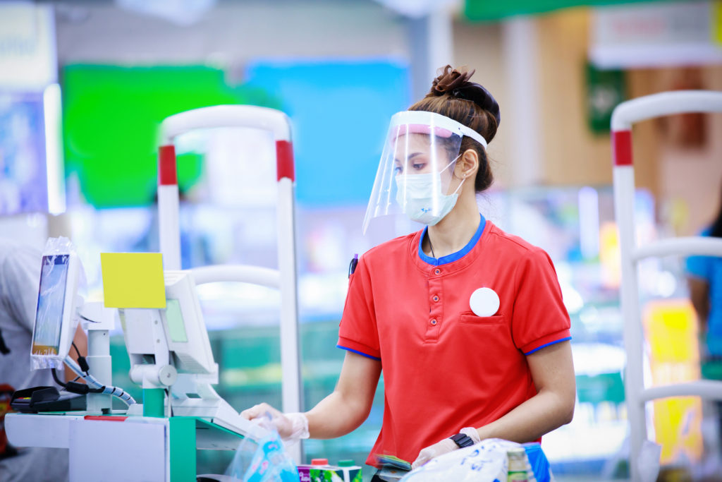 Grocery store cashier wearing a medical mask and face shield.