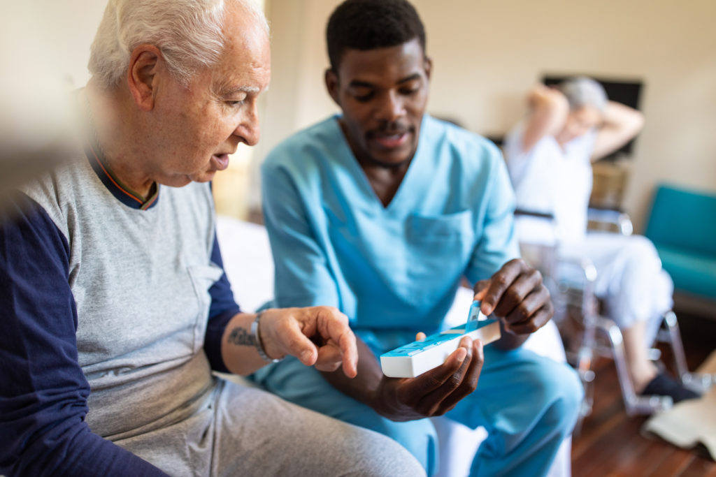 A personal support worker handing medication to an elderly man.