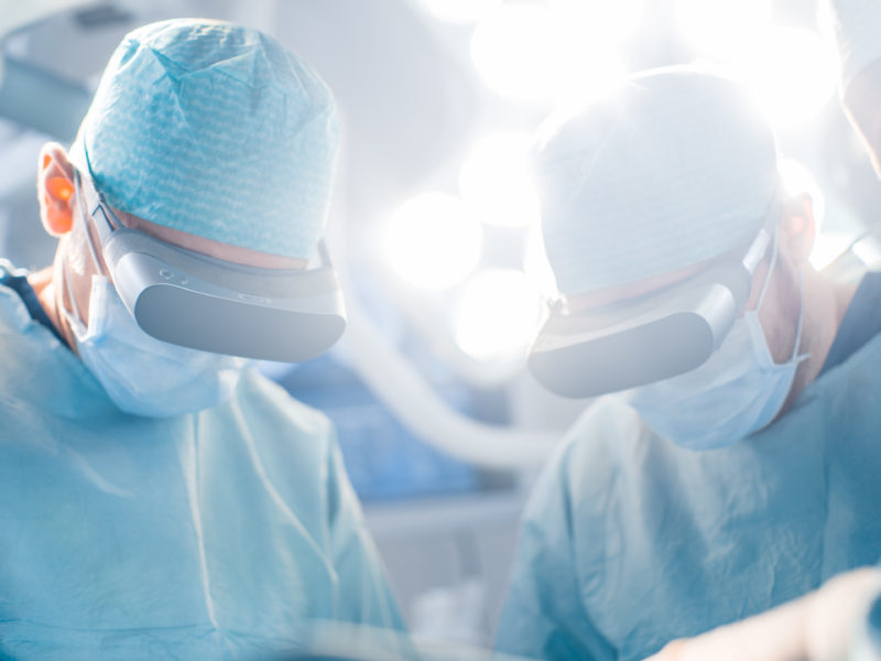 Close-up Shot of a Surgeon Perform State of the Art Surgery in High Tech Hospital using Augmented Reality Glasses. Doctors and Assistants Working in Operating Room.