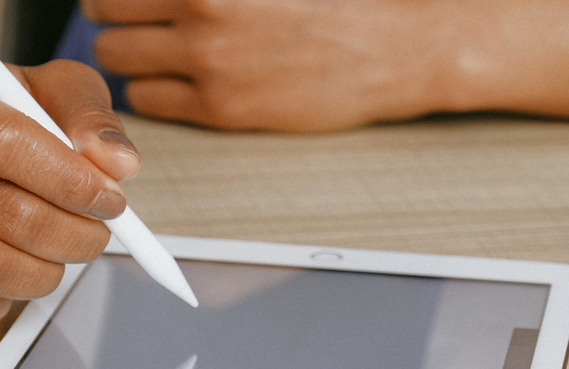 hand holding a stylus and writing on a tablet