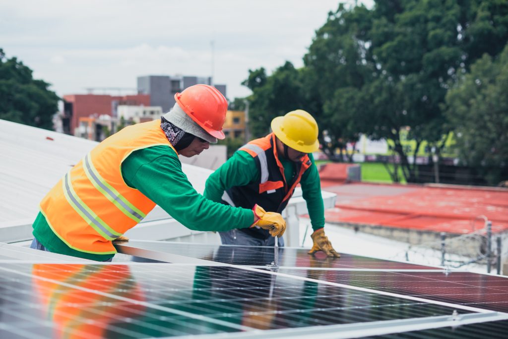 Two construction workers in hardhats installing a solar panel for the net-zero economy