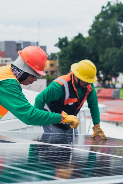 Two construction workers in hardhats installing a solar panel