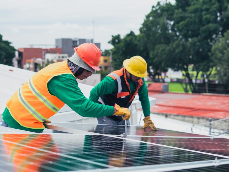 Two construction workers in hardhats installing a solar panel