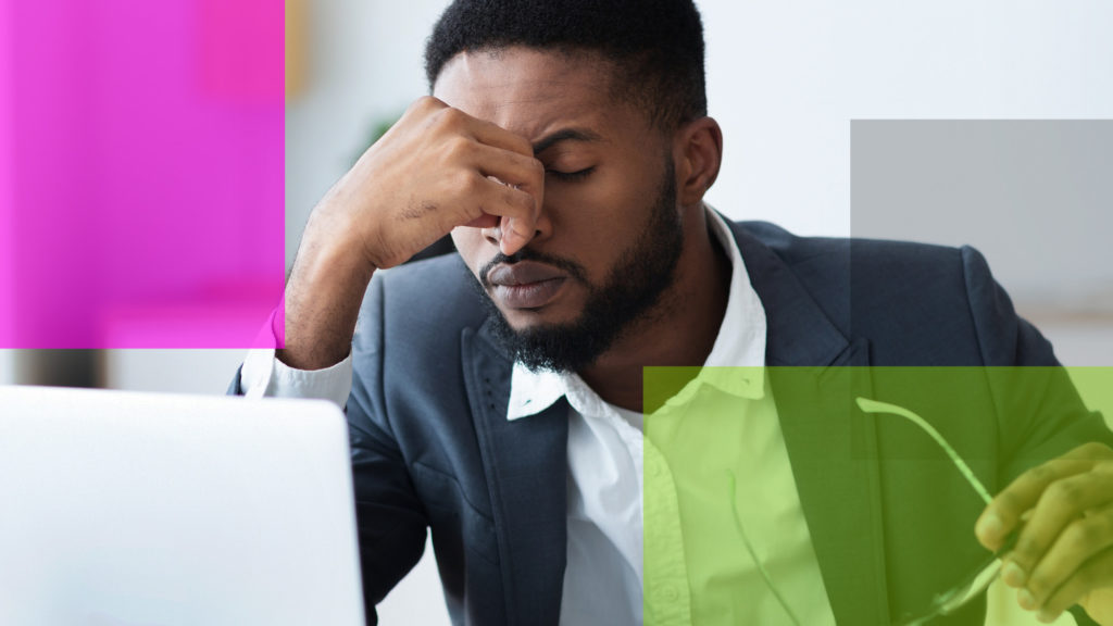 Man with furrowed brows and had massaging bridge of his nose while in front of an opend laptop