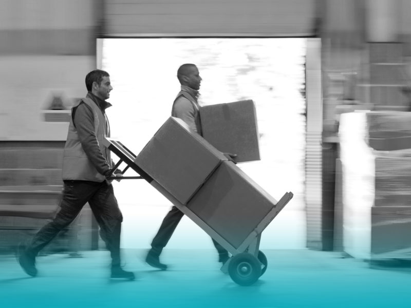 Two workers moving a large cardboard box each on a dolly
