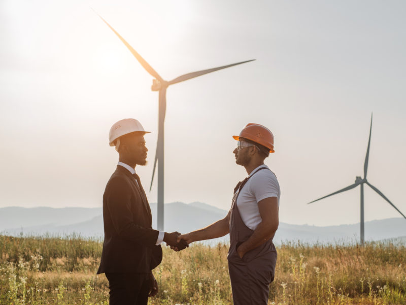 Colleagues shaking hands with wind turbines on background